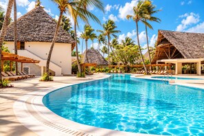 Un resort con una amplia piscina, palmeras y edificios con techo de paja.