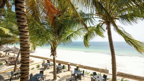 Ein Restaurant direkt am Strand mit Terrassenplätzen, Palmen und Blick auf das Meer.