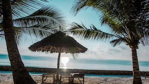 Ein Strand mit einem Strohdachschirm, Holzstühlen und Palmen.