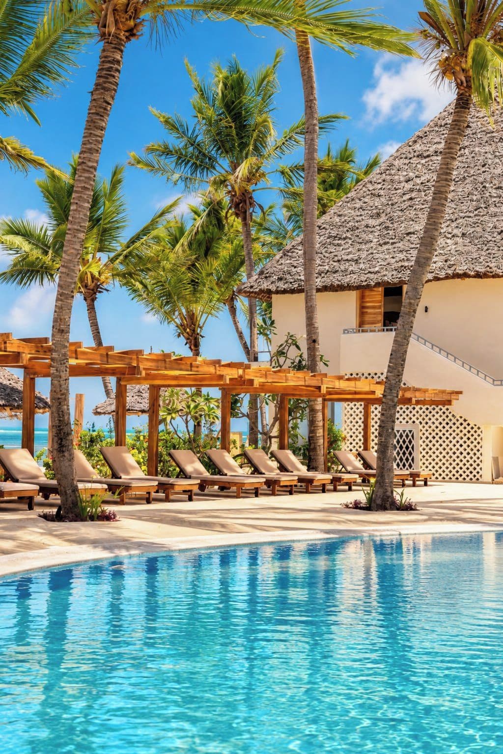 A pool area with lounge chairs and a thatched-roof building.