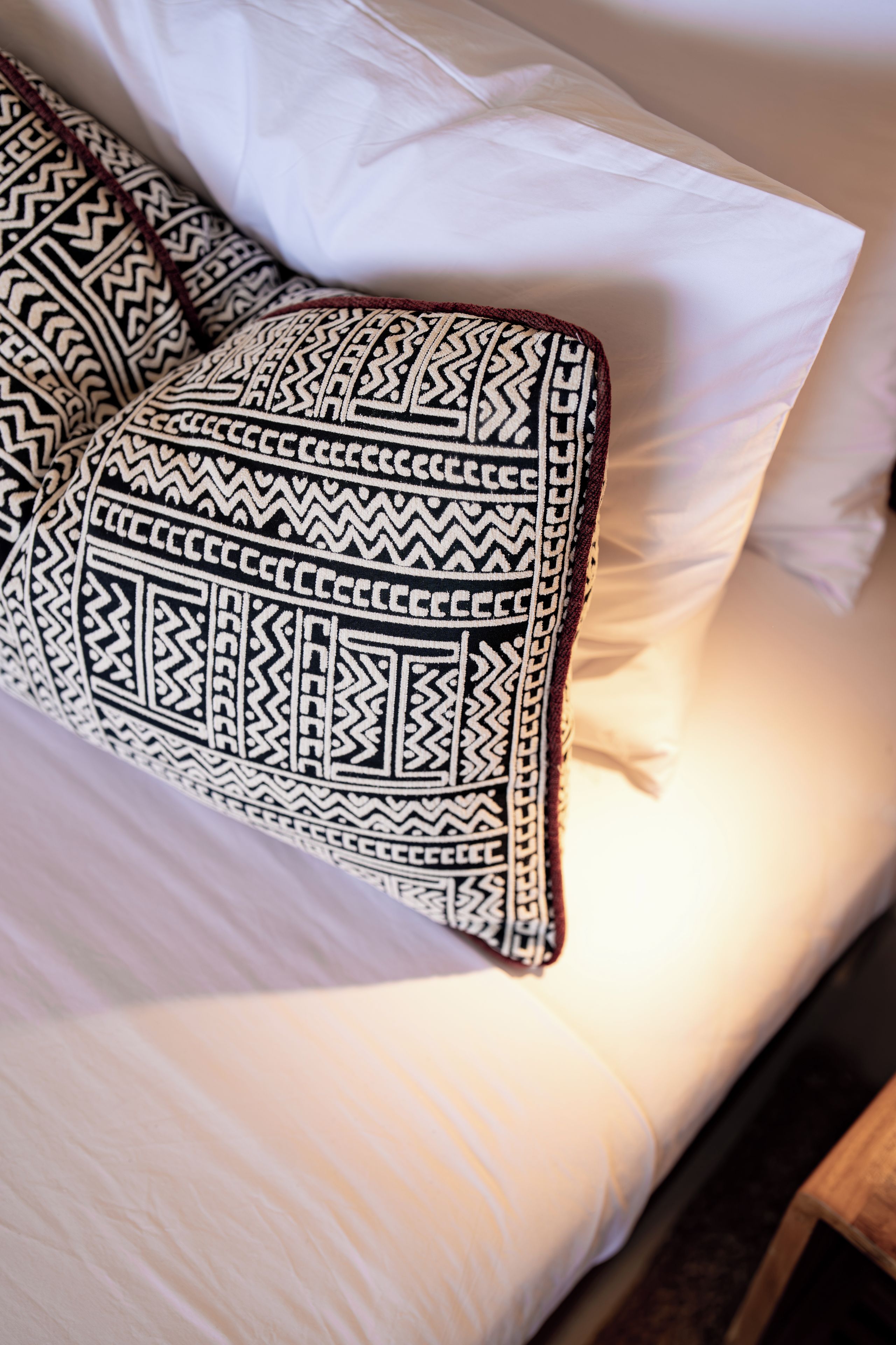 Una cama con ropa de cama blanca y un almohadón estampado.