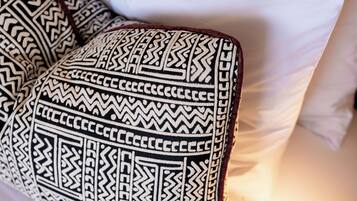 Una cama con ropa de cama blanca y un almohadón estampado.