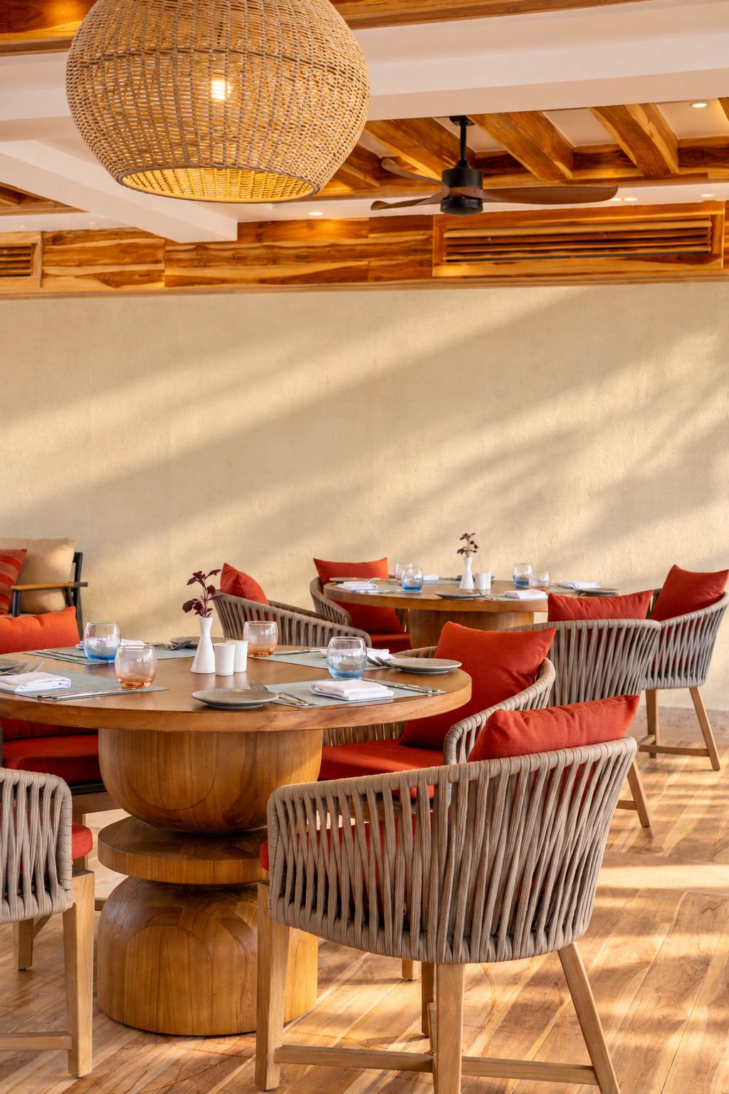 A restaurant with round tables, wicker chairs, and a large woven light fixture.