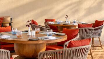 Un restaurant avec des tables rondes, des chaises en osier et un grand luminaire tressé.