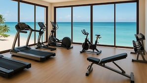 Ein Fitnessraum mit unterschiedlichen Trainingsgeräten und großen Fenstern mit Blick auf einen Strand.