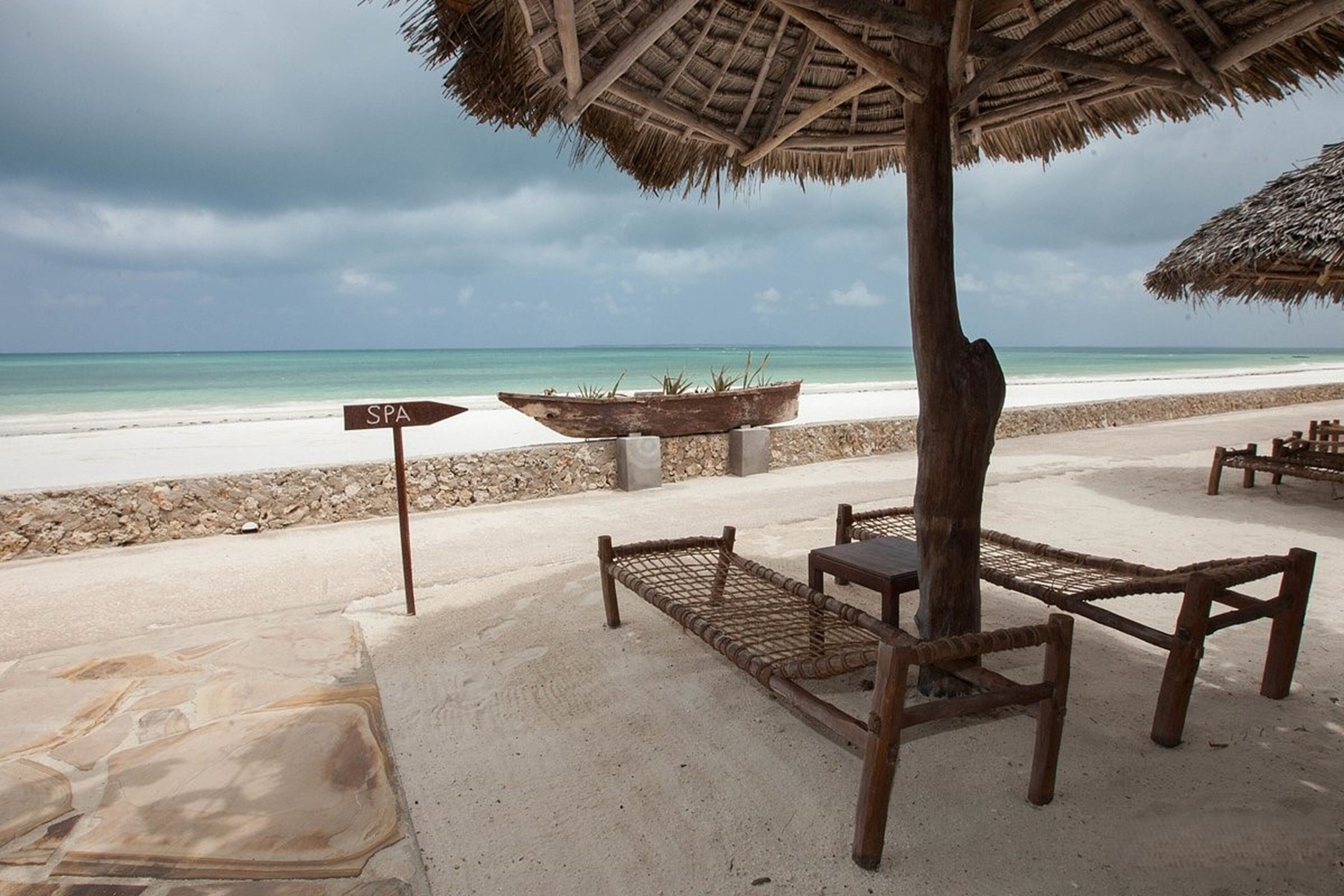 Una playa con una sombrilla de paja, un letrero de spa y un banco de madera.