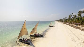 Una playa con agua turquesa cristalina, palmeras y barcos con velas.