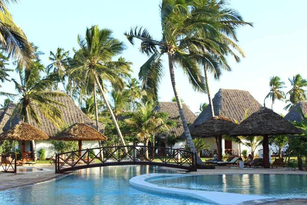 A pool area with thatched-roof structures and palm trees.