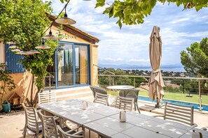 Une terrasse avec une table et des chaises, un parasol et une vue sur une piscine et un jardin.