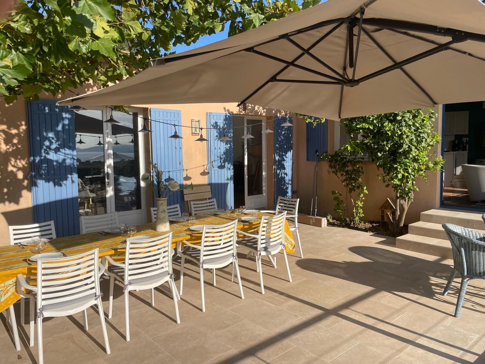 Une terrasse extérieure avec une table dressée pour le repas, entourée de chaises, et protégée par un grand parasol.