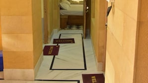 A narrow hallway with a bed at the end, two welcome mats on the floor, and a light fixture on the ceiling. - Golden Home Hotel By GRB (Jaisalmer)