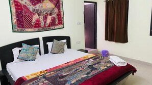 A bedroom with a bed, pillows, a blanket, a tapestry, a curtain, and a bucket. - Golden Home Hotel By GRB (Jaisalmer)