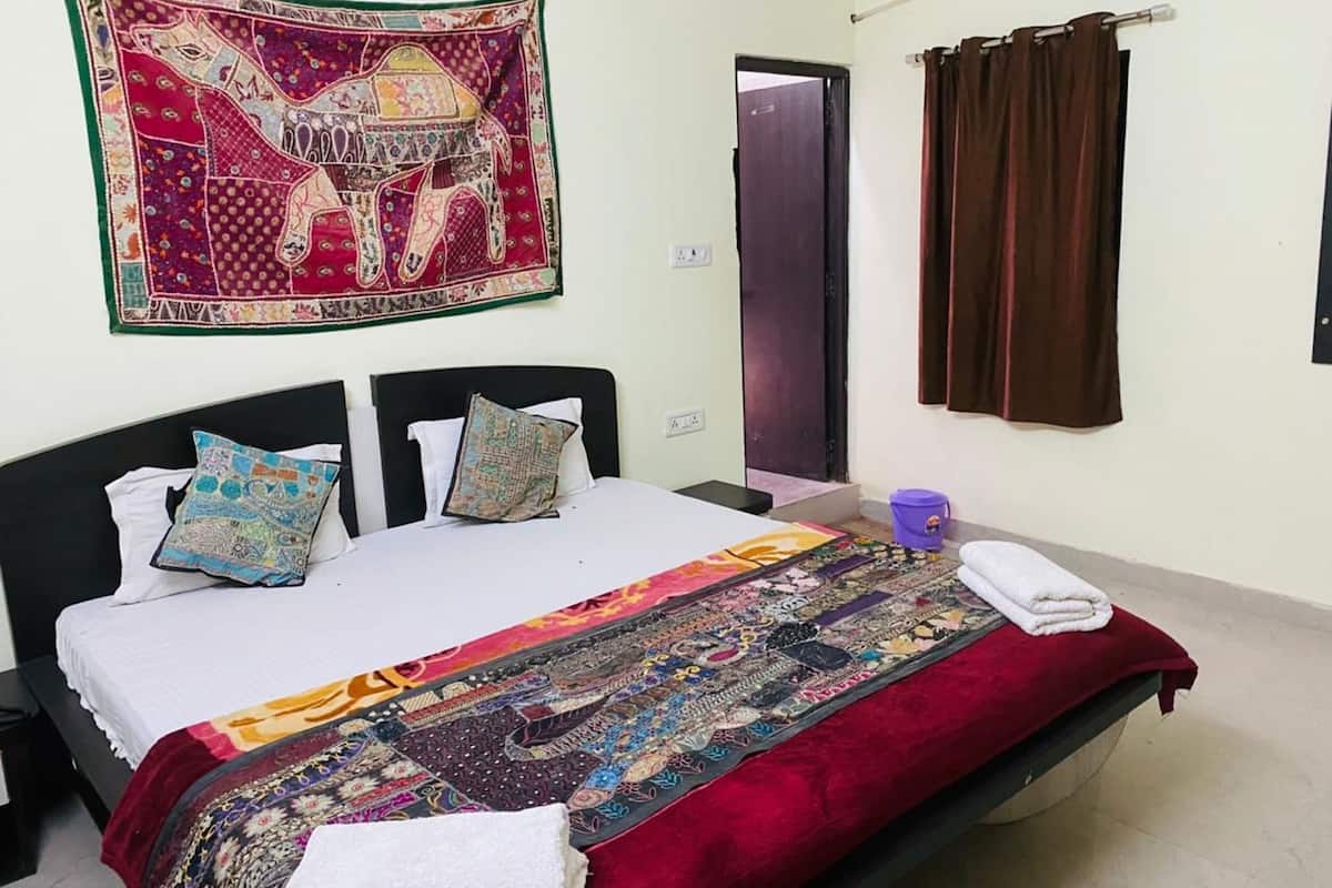 Une chambre à coucher avec un lit, des oreillers, une couverture, une tapisserie, un rideau et un seau.