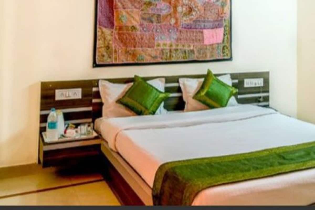 Une chambre d’hôtel avec un lit, une table de chevet, une courtepointe accrochée au mur et un tableau au-dessus du lit.
