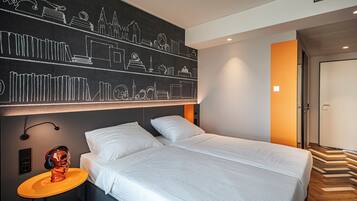 Ein modernes Hotelzimmer mit einem großen Bett, einem Nachttisch mit Lampe und einer Wand mit Stadtbild-Mural.