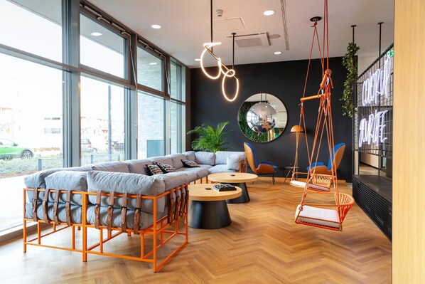 A modern interior with a sofa, two round tables, a hanging chair, and large windows. - LOGINN Hotel Köln Airport (Cologne)