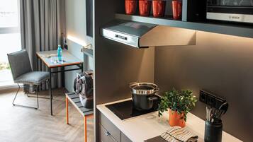 A modern kitchen with a Bosch microwave, a stove, and a sink. There is a small table with a chair and a potted plant.