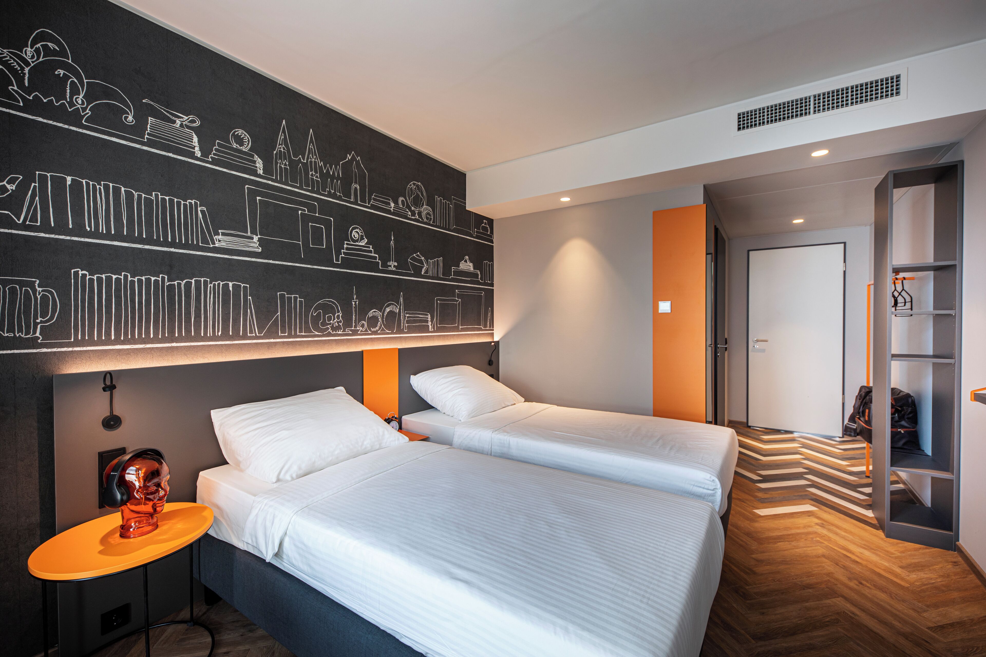 A modern hotel room with two beds, a chalkboard wall, and a wooden floor.