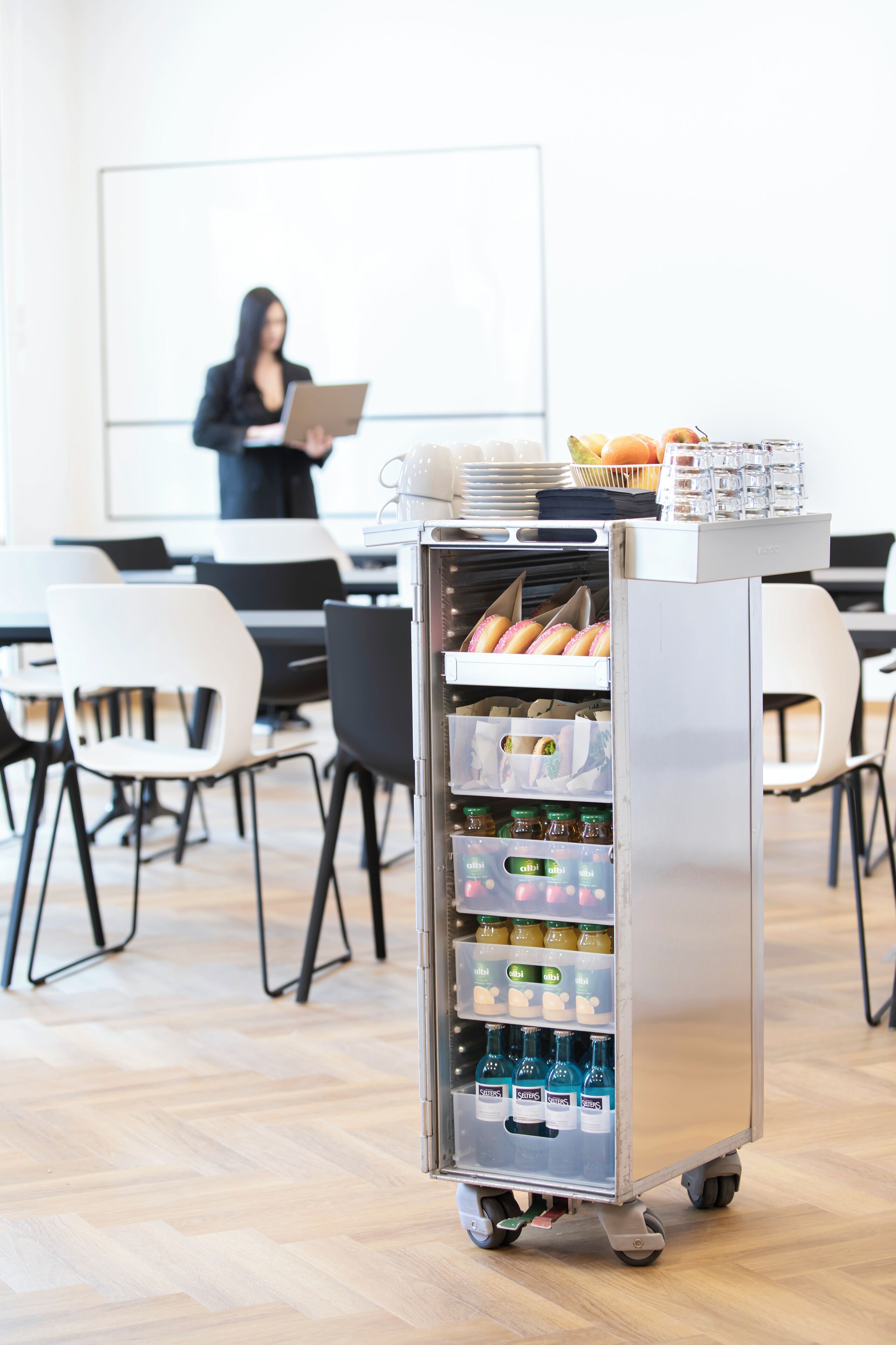 A refrigerated beverage cart in a modern office setting with a whiteboard and chairs.