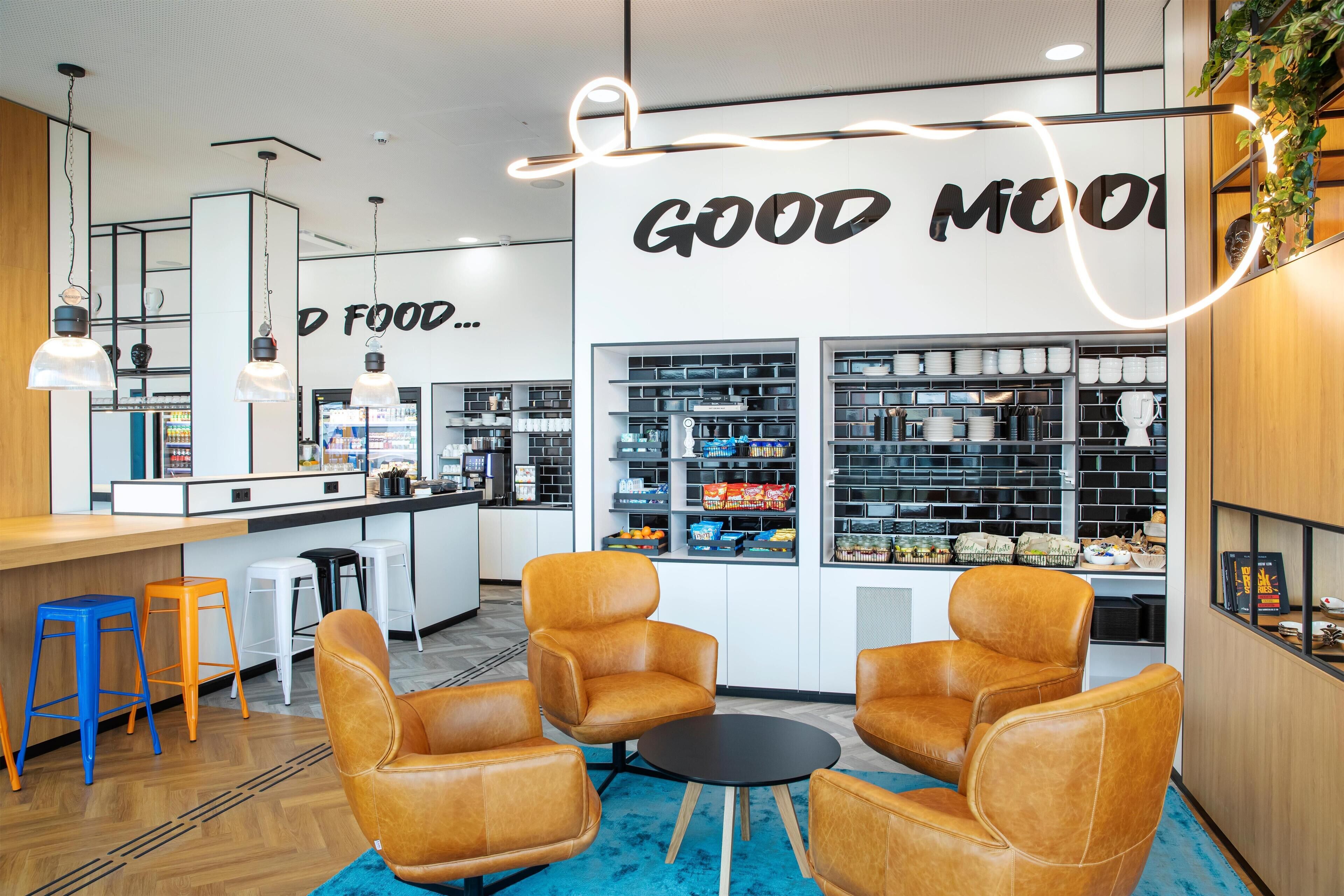 A modern cafe interior with leather chairs, a bar area, and shelves stocked with food items.