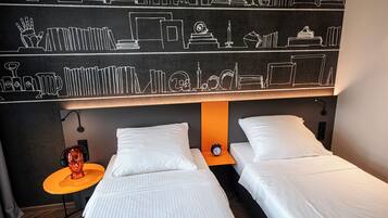 Habitación de hotel con dos camas, una pared de pizarra con dibujos educativos, una mesita naranja pequeña y una escultura roja.