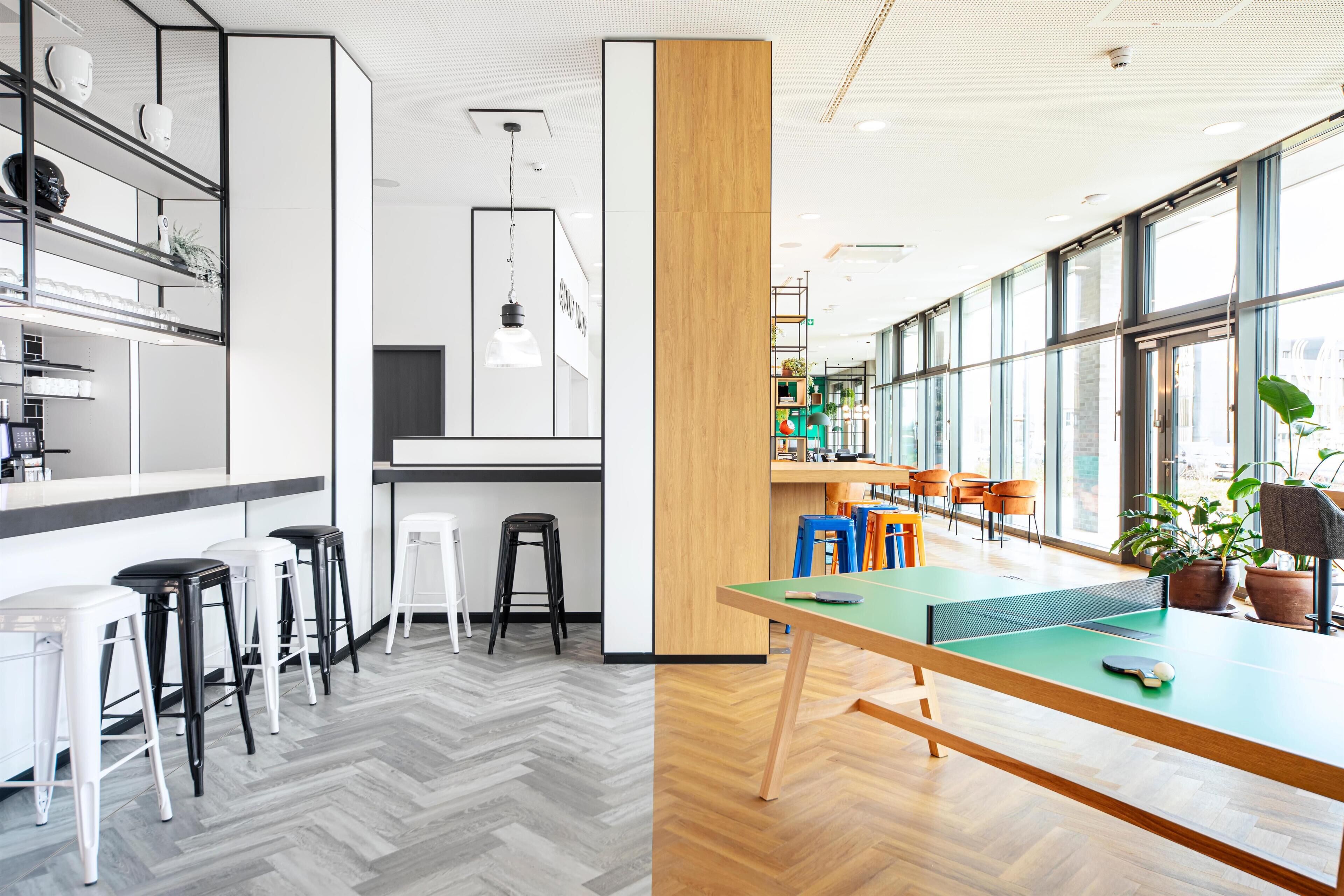 A modern indoor space with a ping pong table, bar stools, and a counter area.