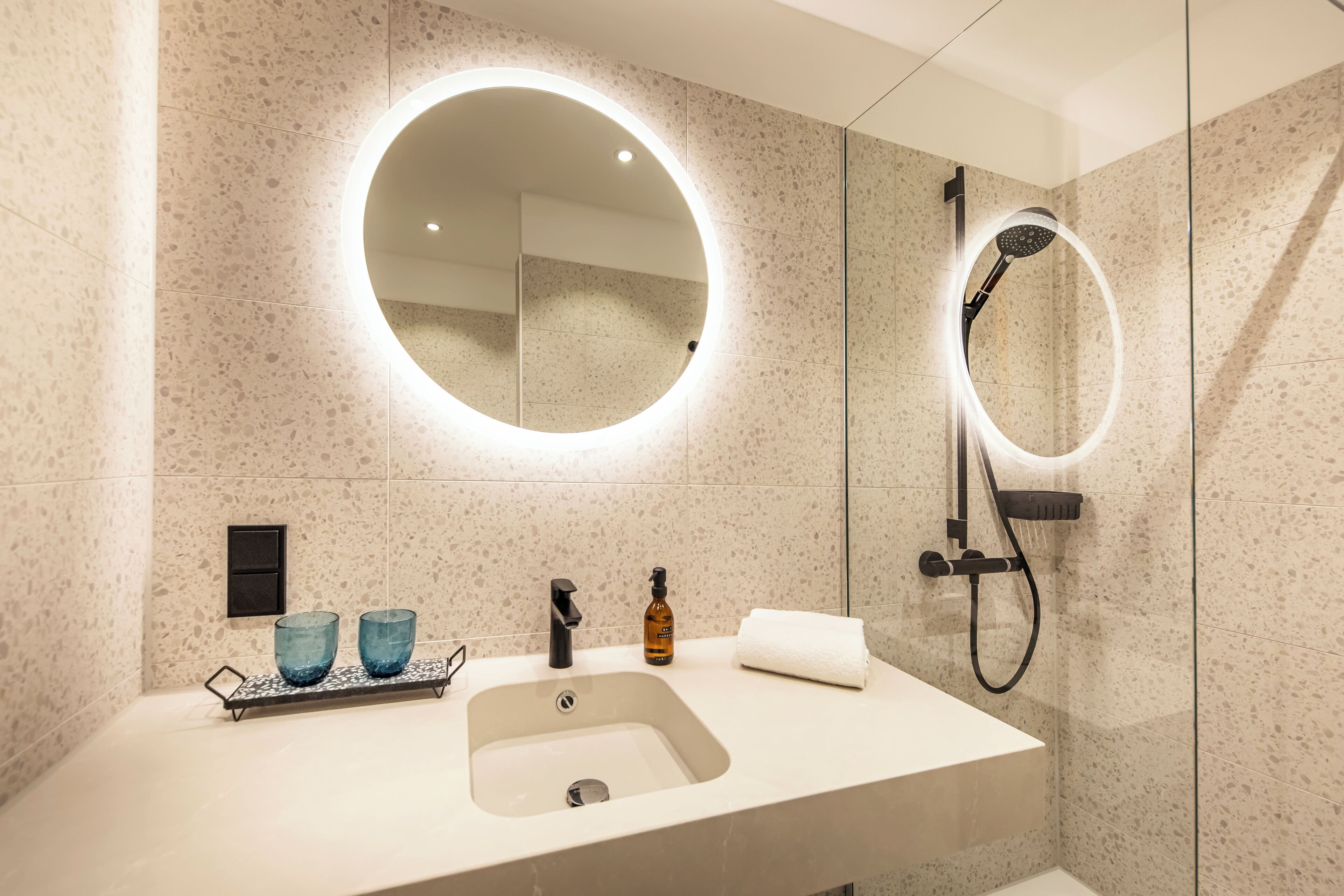 A modern bathroom with a large sink, two blue glass containers, a soap dispenser, and a towel.