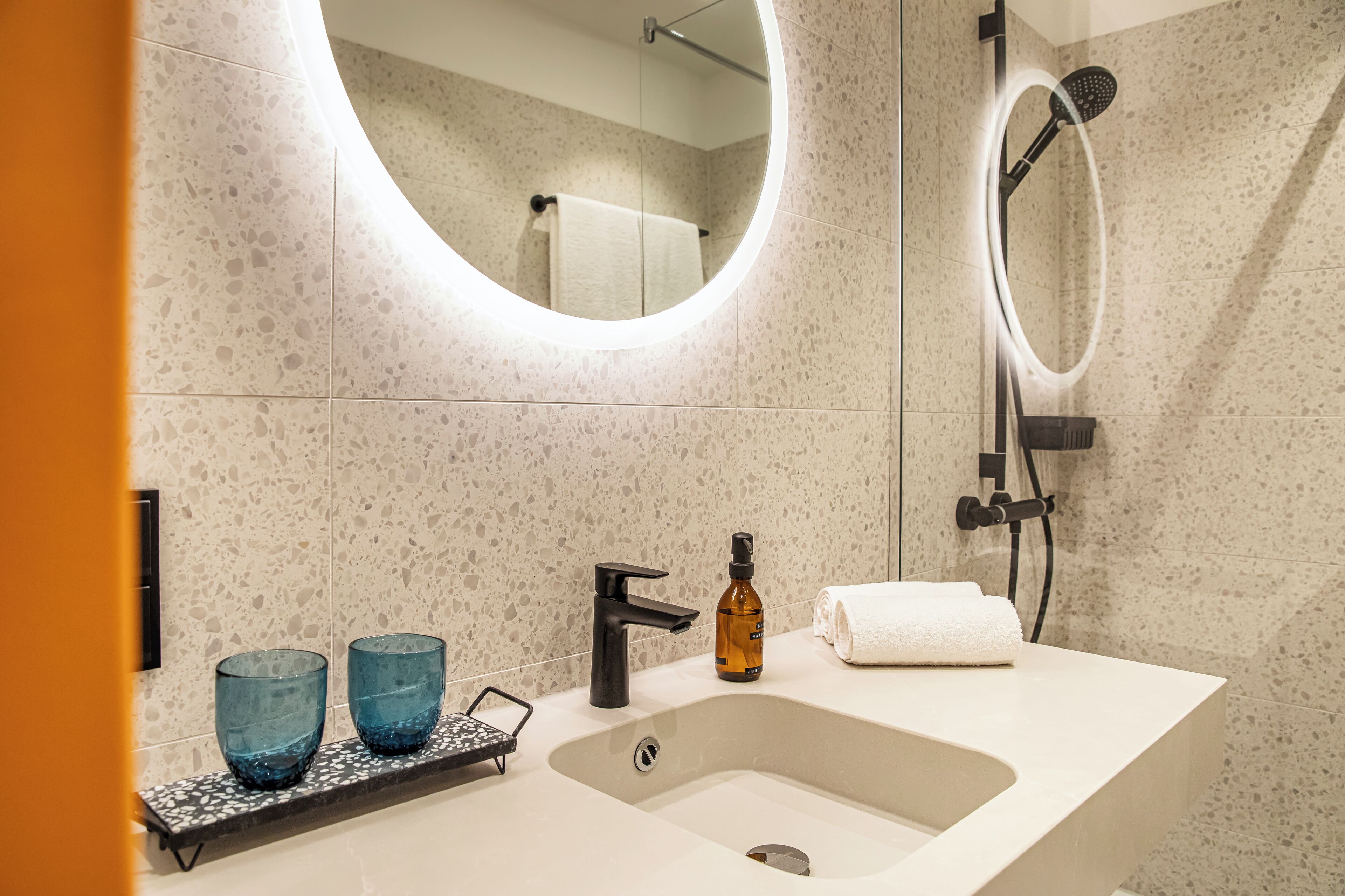 A modern bathroom with a freestanding sink, two blue glass vases, a black faucet, and a handheld showerhead.