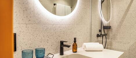 A modern bathroom with a freestanding sink, two blue glass vases, a black faucet, and a handheld showerhead.