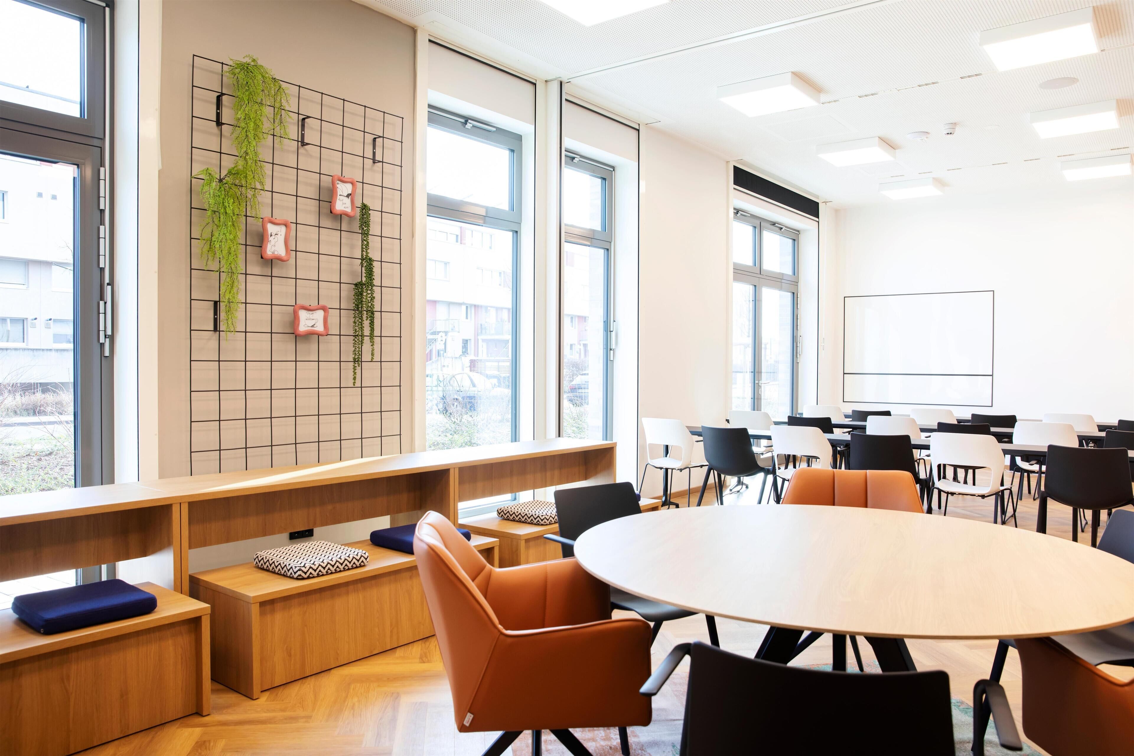 A modern conference room with a round table, comfortable seating, a grid wall with plants, and large windows.