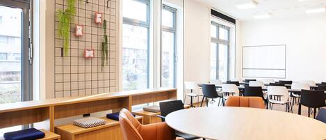 A modern conference room with a round table, comfortable seating, a grid wall with plants, and large windows.