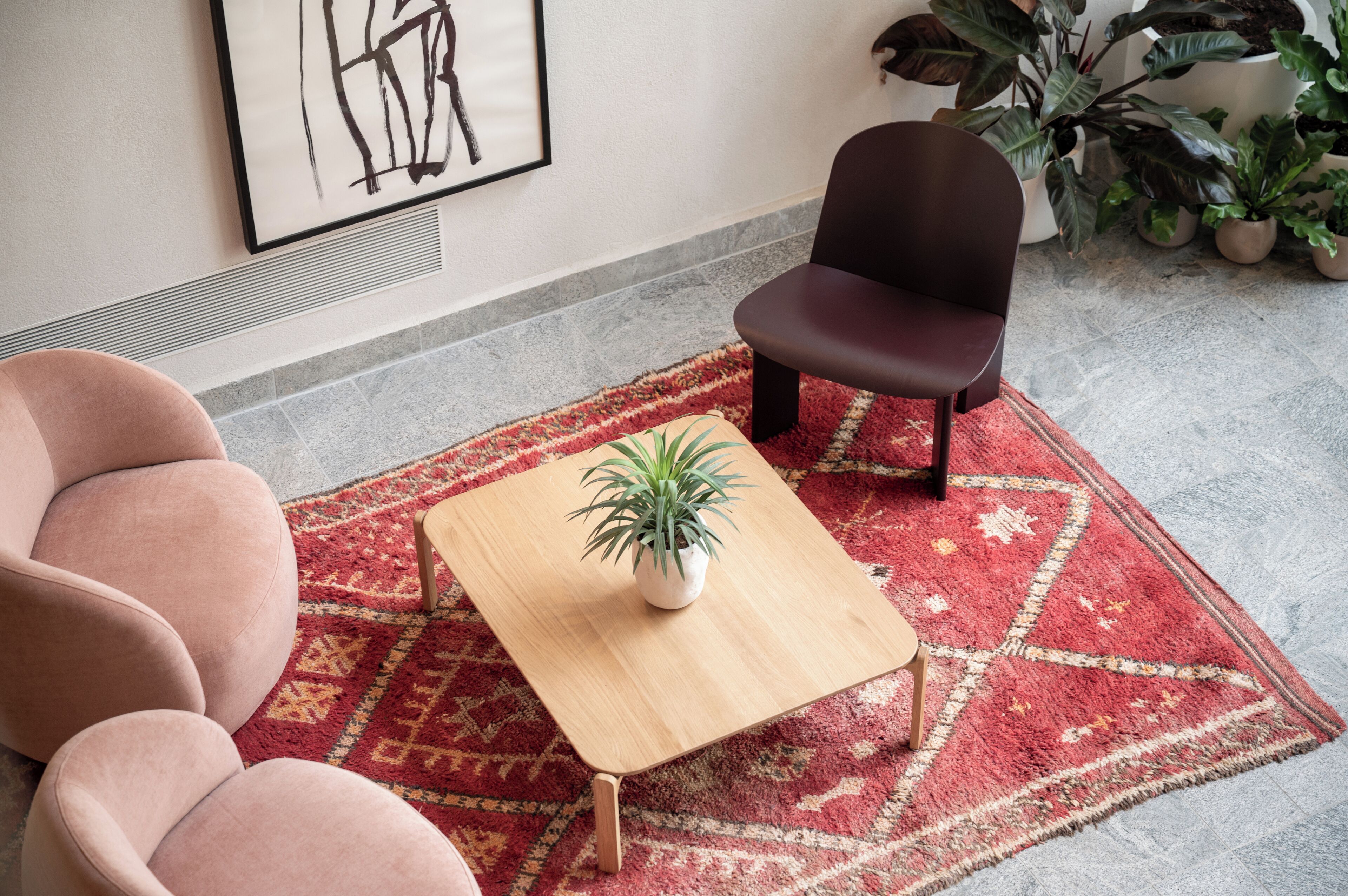 A modern living room with a red patterned rug, a wooden coffee table with a potted plant, and a dark brown chair.