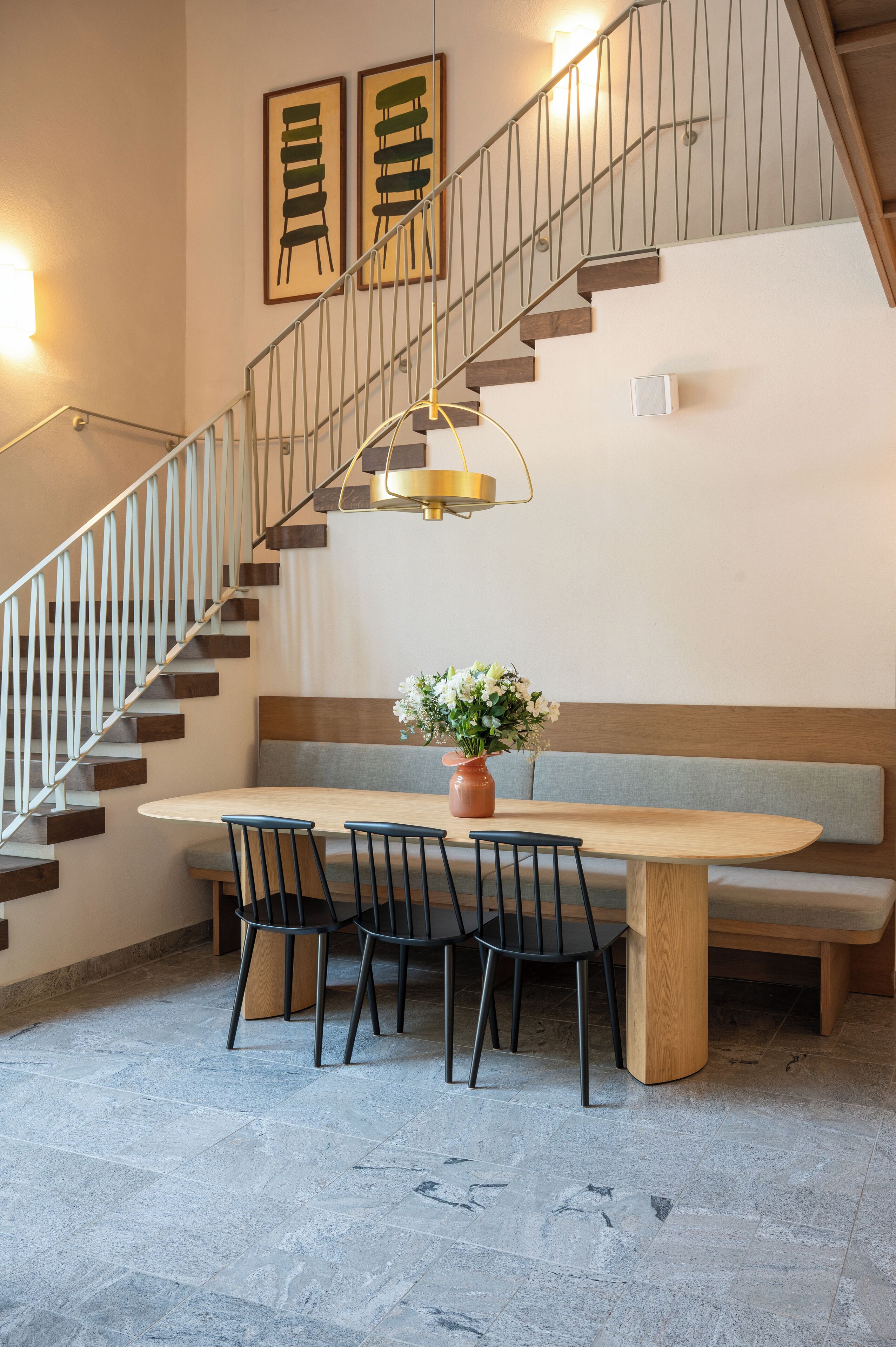 A dining area with a wooden table, four chairs, a bench, and a staircase with a metal railing.