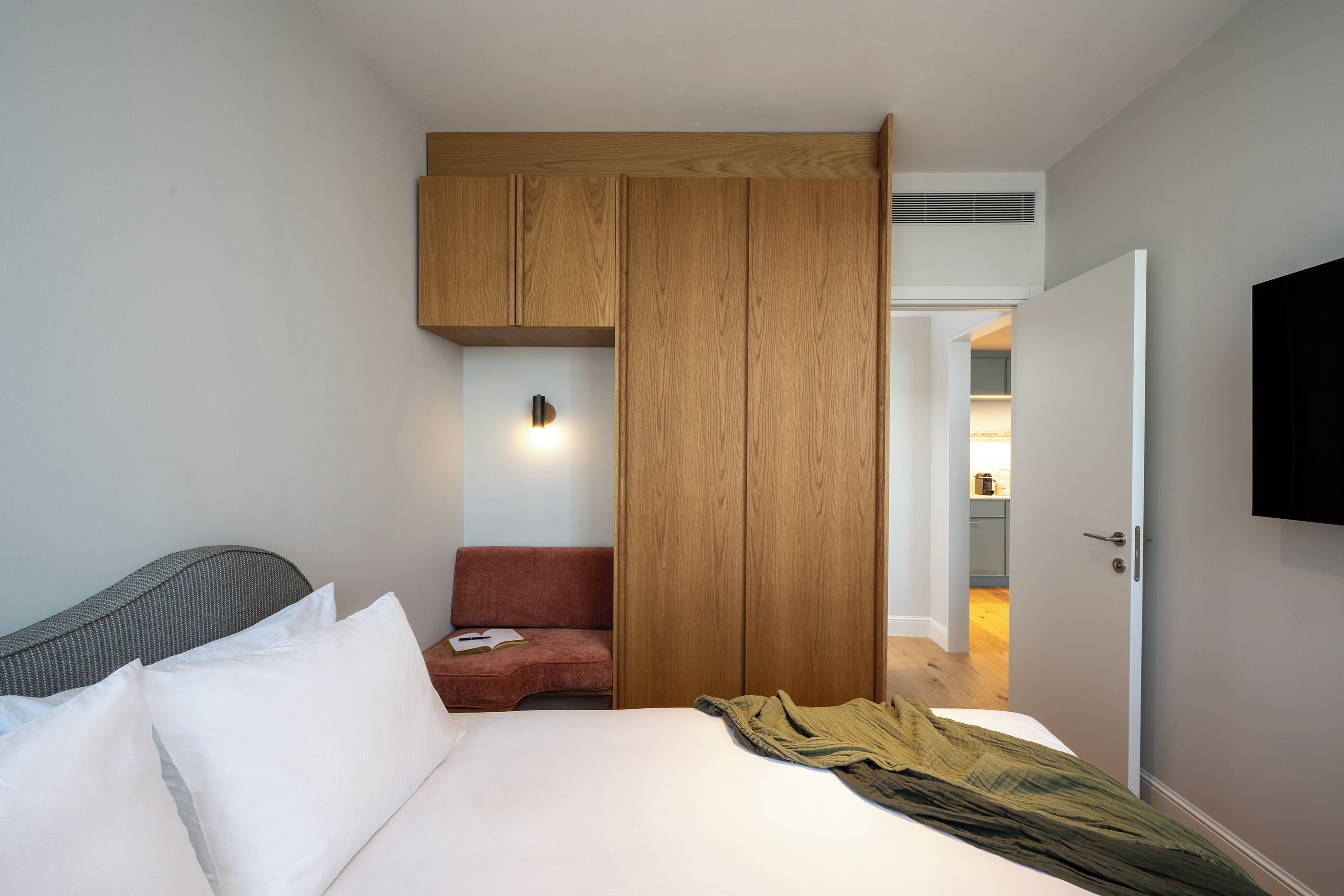 Une chambre d’hôtel avec un lit, une chaise rouge, une armoire en bois et un téléviseur fixé au mur.