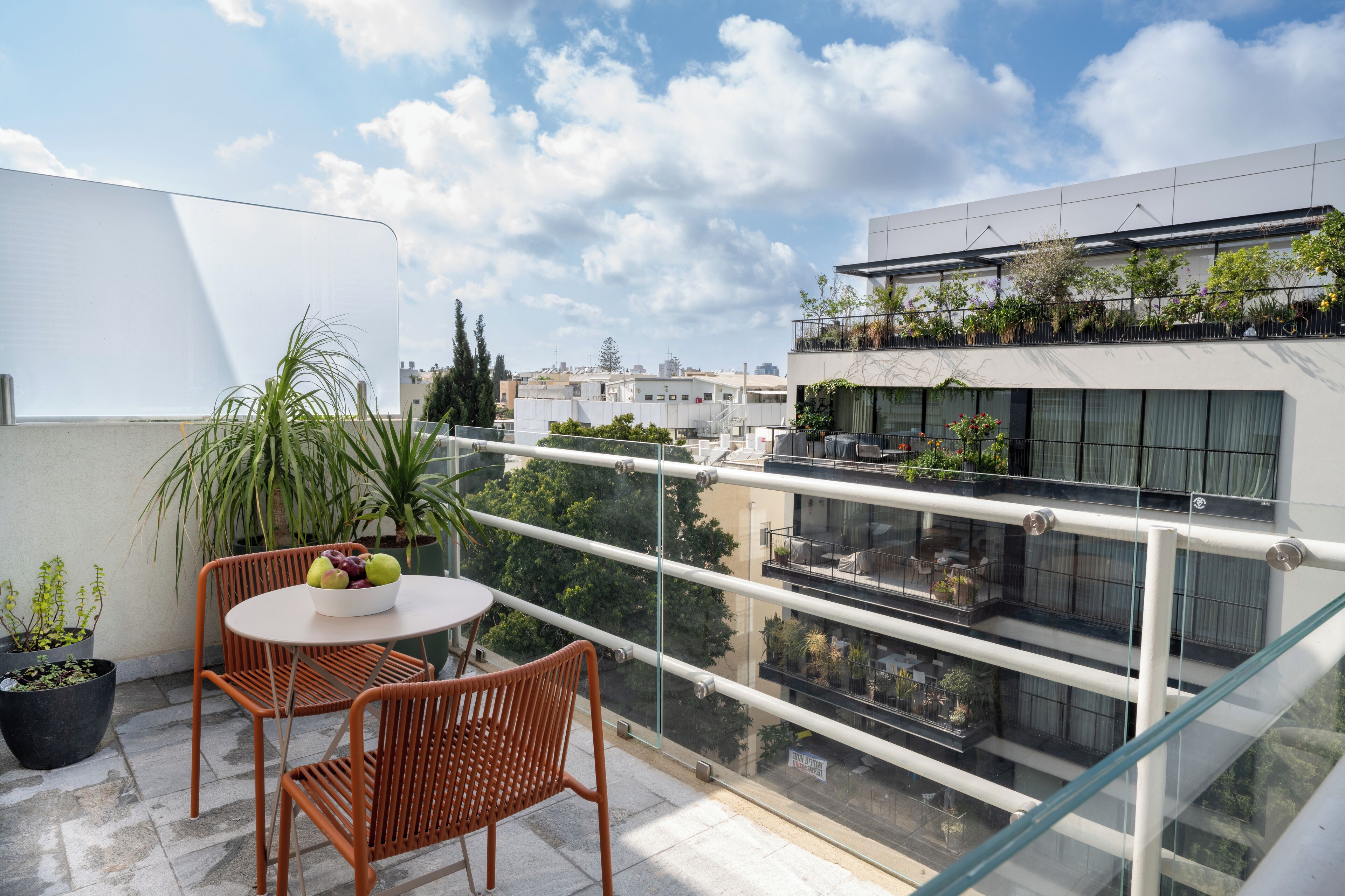 A balcony with a table and chairs, potted plants, and a view of a modern building with balconies.