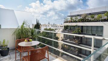 A balcony with a table and chairs, potted plants, and a view of a modern building with balconies.