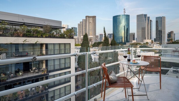 Eine Dachterrasse mit Außenmöbeln, Blick auf eine Stadtsilhouette und ein modernes Gebäude mit Balkonen.