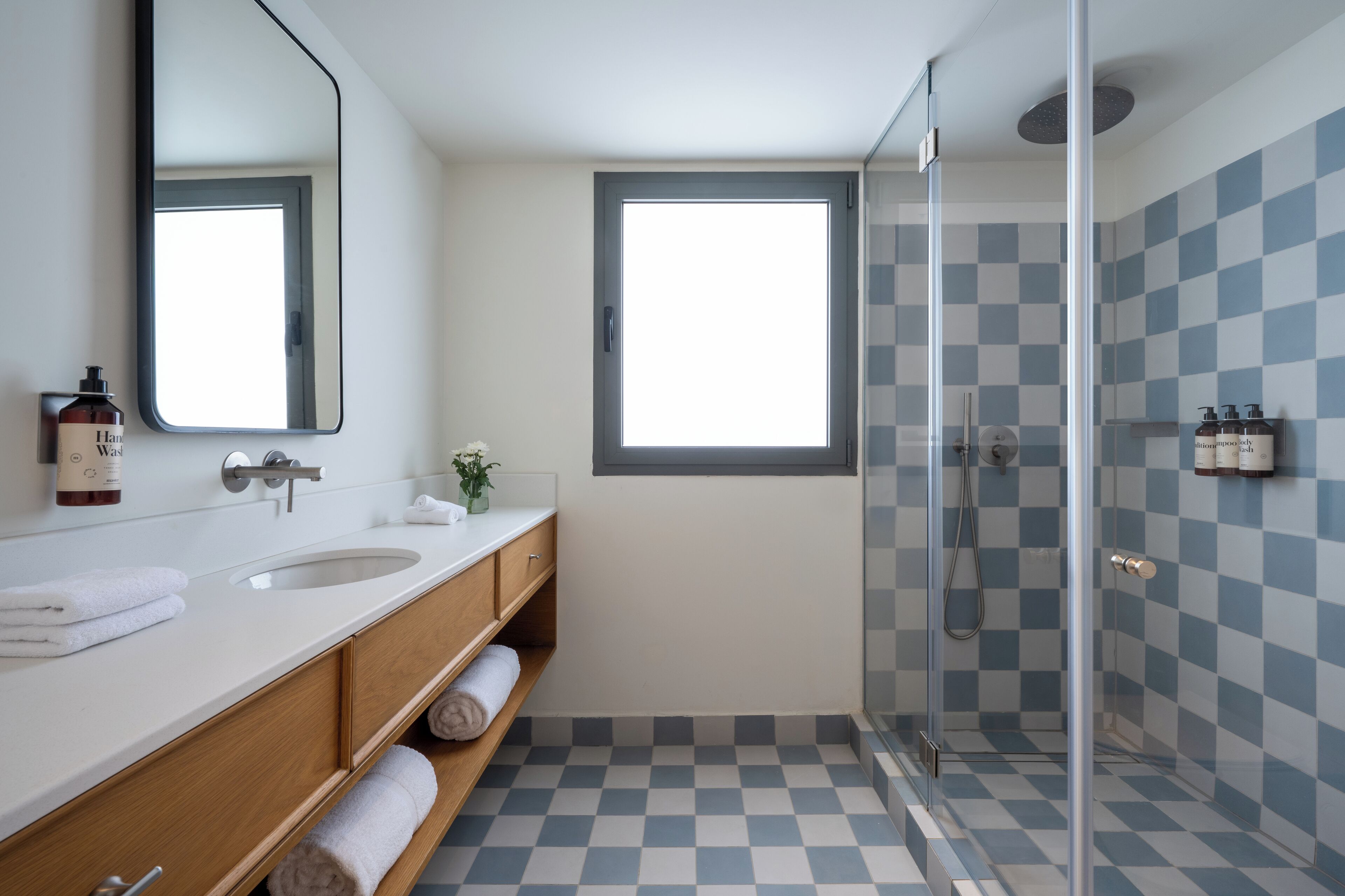 Une salle de bain moderne avec un grand miroir, deux lavabos, une douche et des carreaux de sol à motifs carrés.