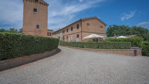 A historic building with a tower, a gravel driveway, and a hedge.