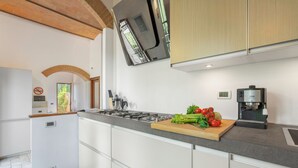 A modern kitchen with white cabinets, a gas stove, a coffee machine, and fresh vegetables on the counter.