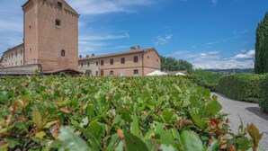 A historic building with a tower and multiple windows, surrounded by lush greenery and a clear sky.