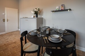Ein Essbereich mit einem runden Tisch, gedeckt für vier Personen, inklusive Teller, Gläsern, Besteck und einer Blumenvase.