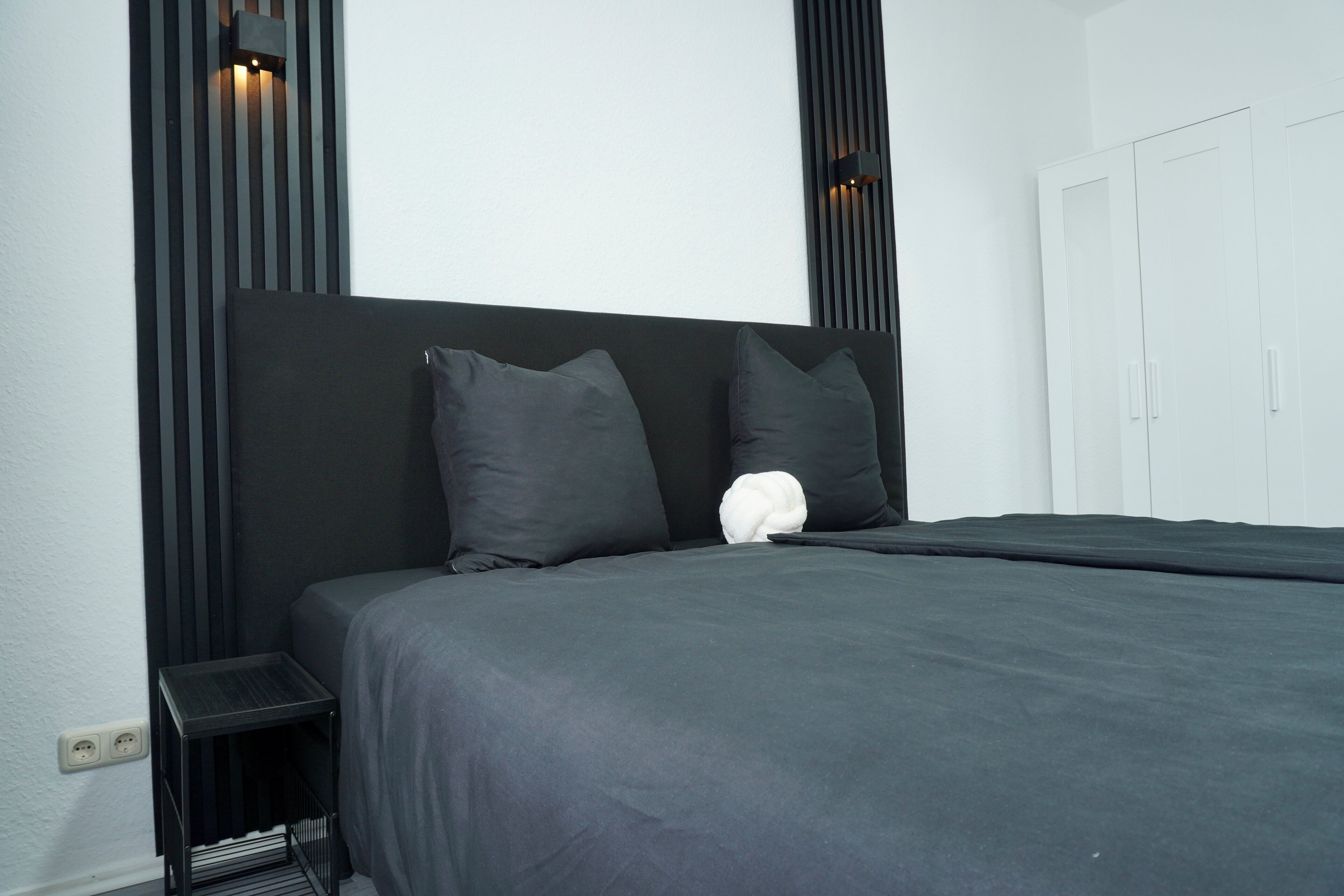 Ein modernes Schlafzimmer mit einem großen Bett, einem dunklen Kopfteil und zwei Wandleuchten.