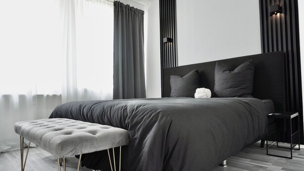 A modern bedroom with a large bed, a grey bench, and a bedside table. - Loft & Living am Geiseltalsee (Braunsbedra)