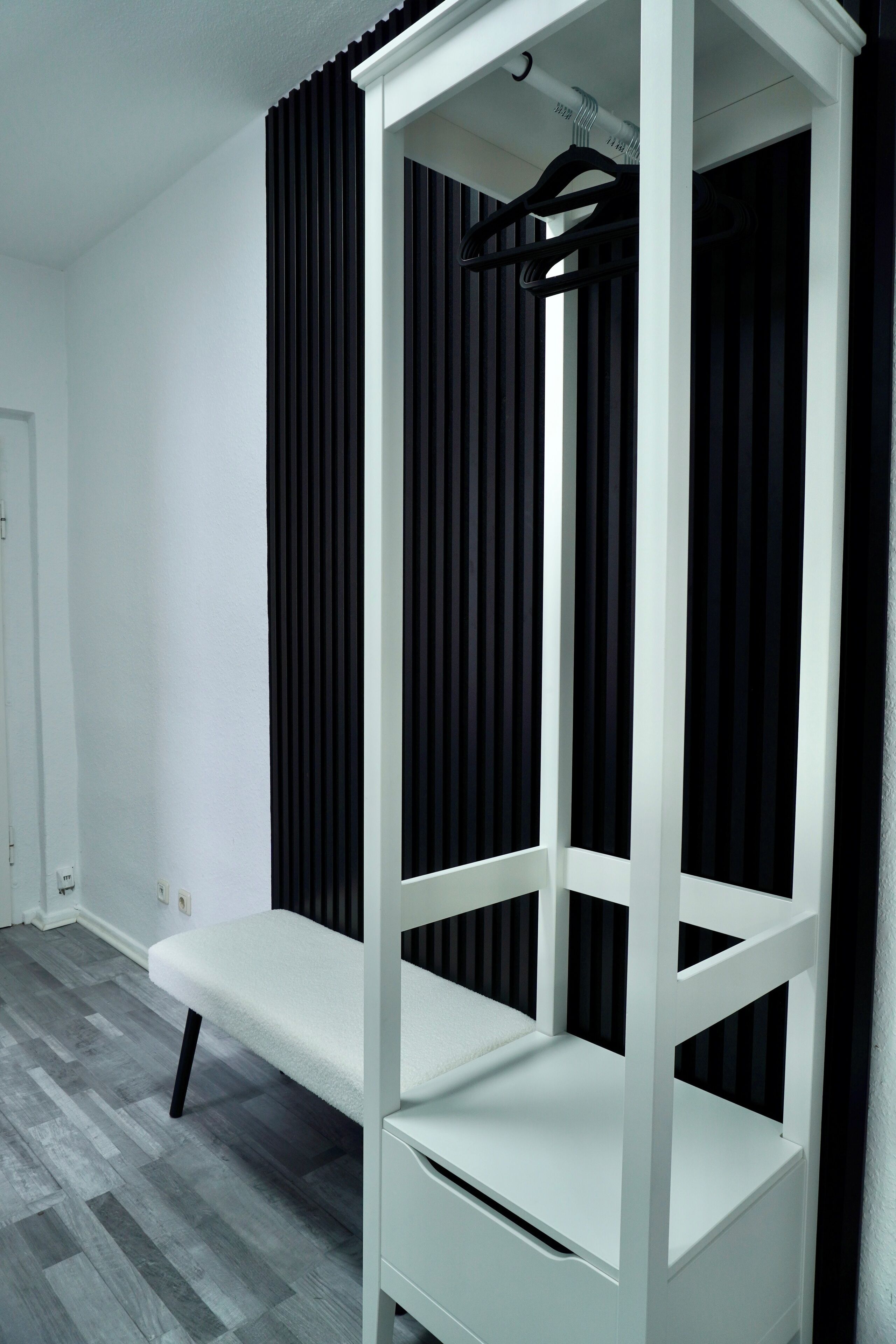 Una cama litera blanca con una banca, persianas verticales negras y una puerta blanca.