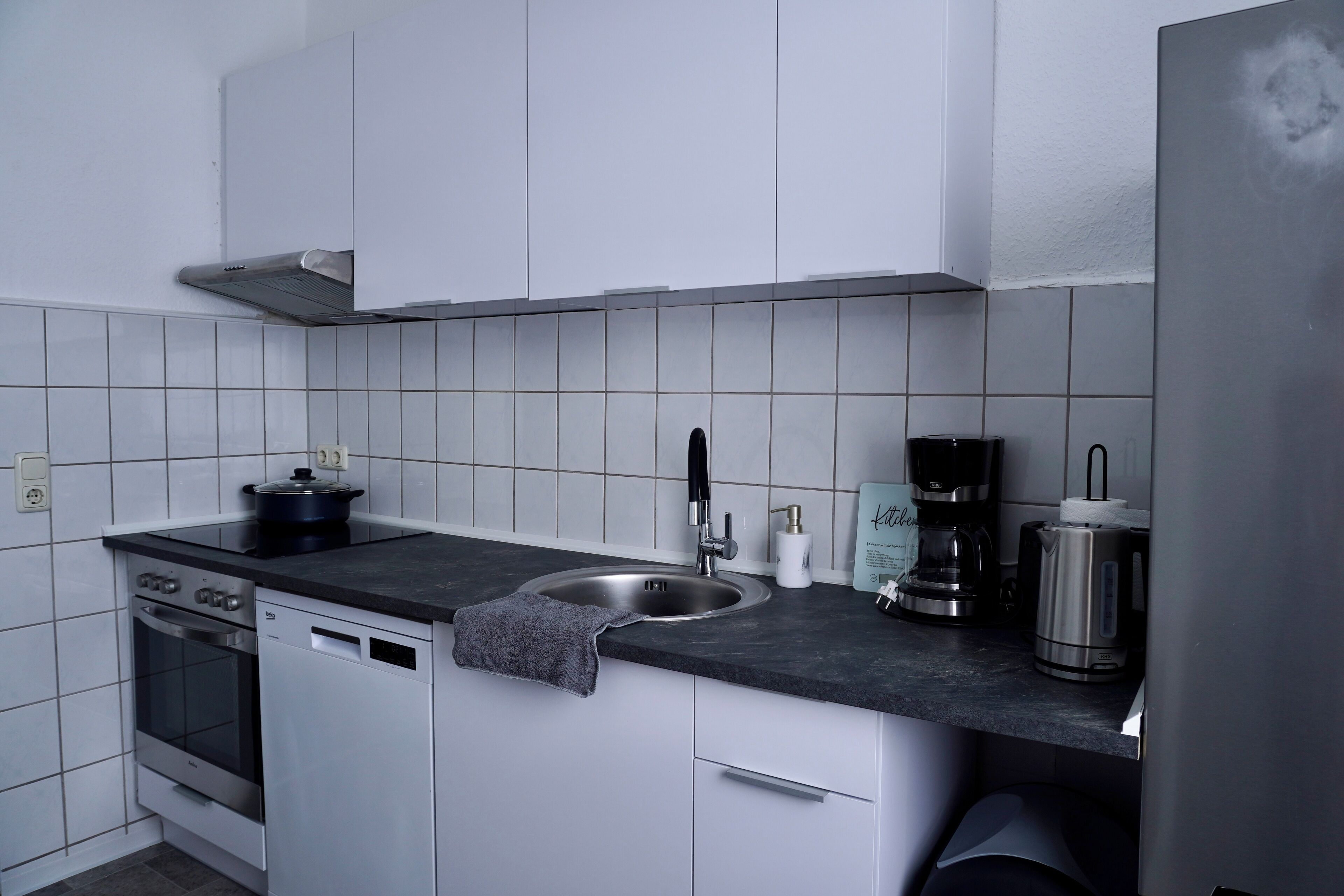 Een moderne keuken met witte kasten, een roestvrijstalen spoelbak, een koffiezetapparaat en een waterkoker.