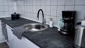 A modern kitchen with a stainless steel sink, black countertop, and a coffee maker. - Loft & Living am Geiseltalsee (Braunsbedra)