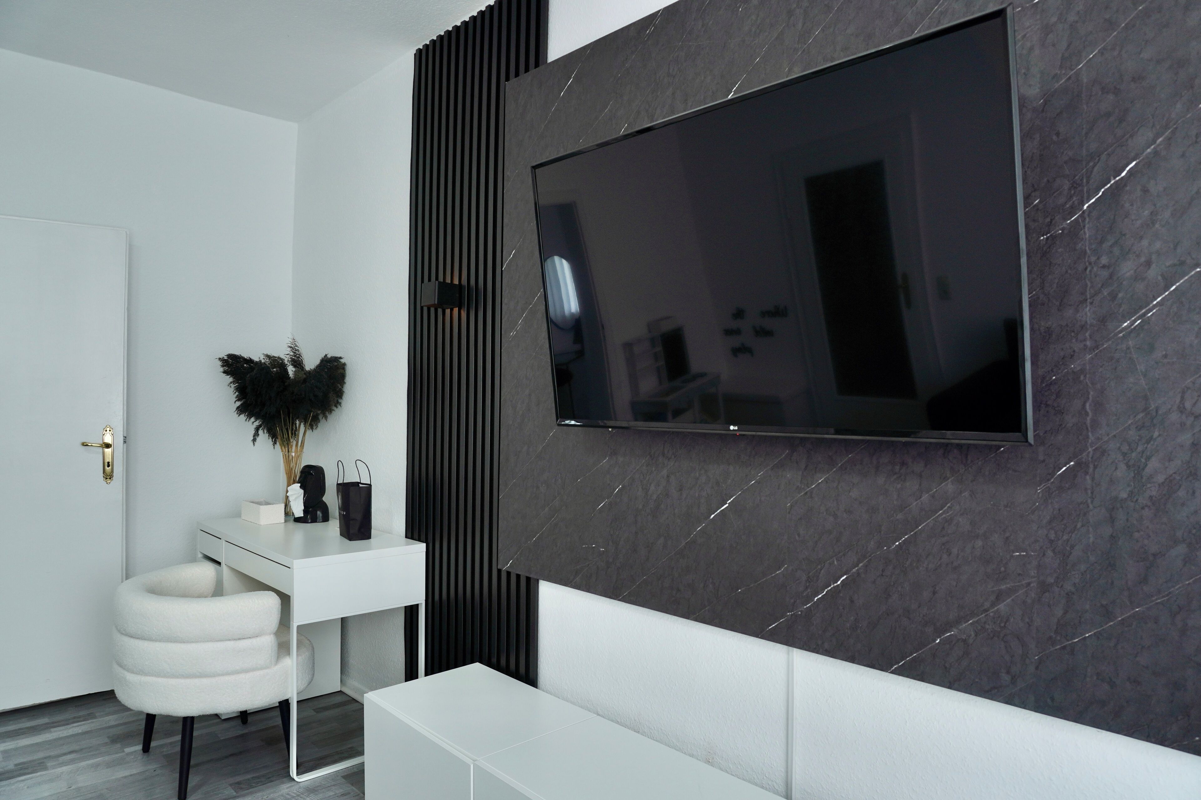 A modern living room with a large flat-screen TV mounted on a dark marble wall, a white console table with decorative items, and a white sofa.