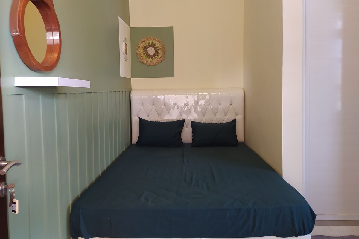 A bedroom with a bed, a mirror, a wall decoration, and a door.