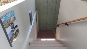 Un escalier orné de carreaux décoratifs et doté d’une rampe, menant à une pièce dont un mur est recouvert d’un revêtement texturé vert et sur lequel est accrochée une affiche.